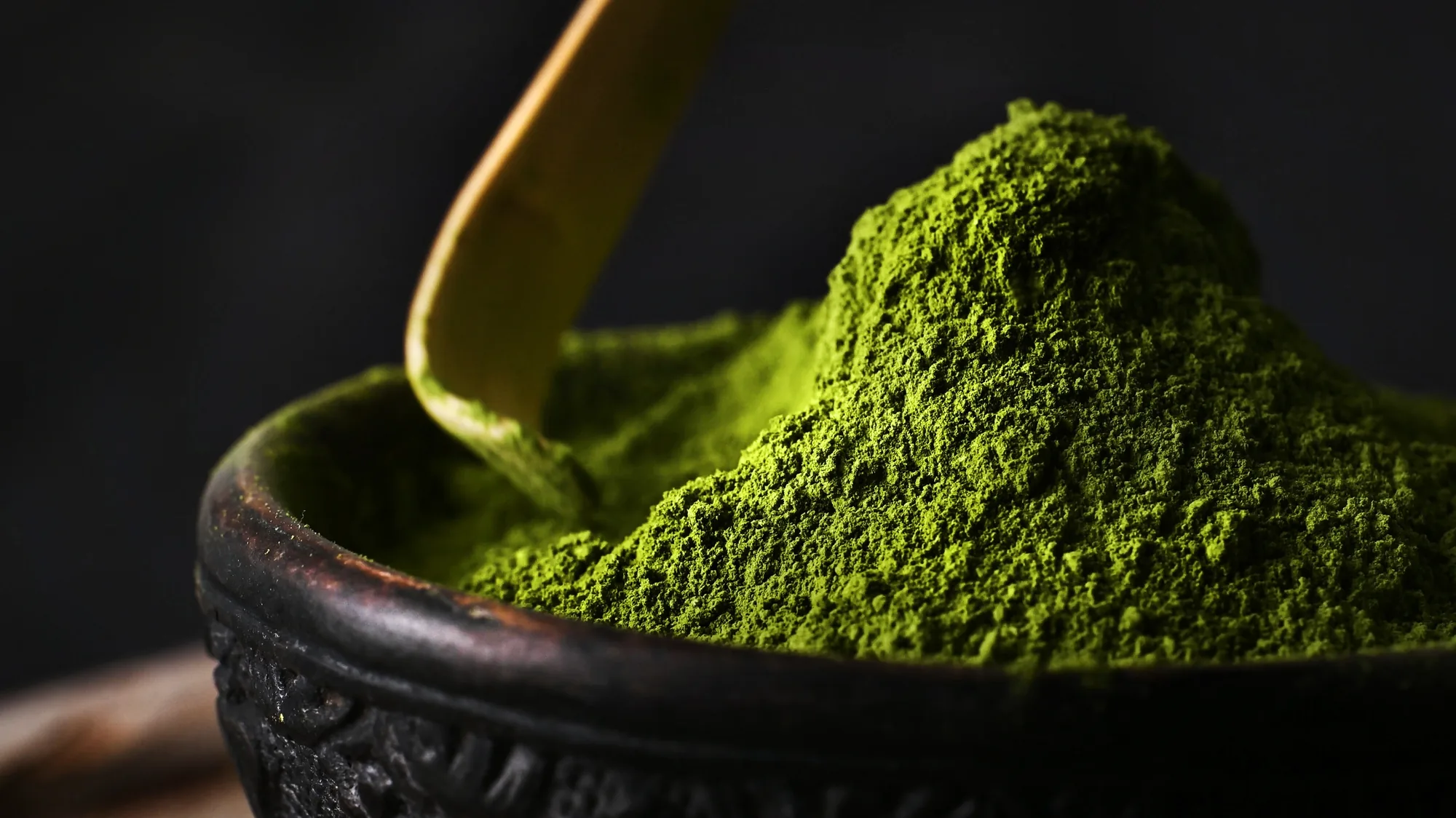 Matcha powder in a dark bowl with a bamboo scoop